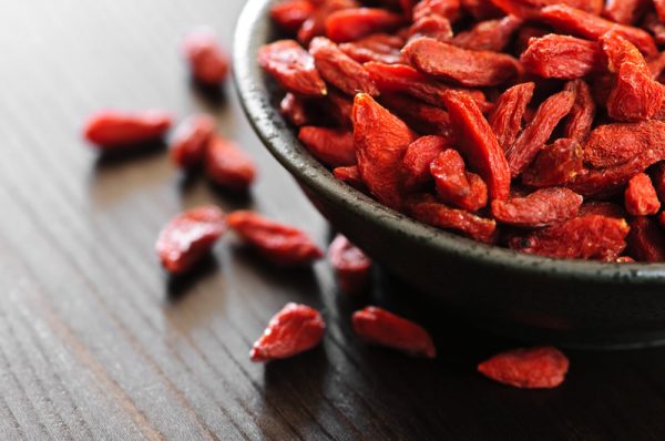A bowl of dried goji berries sits on a wooden surface.