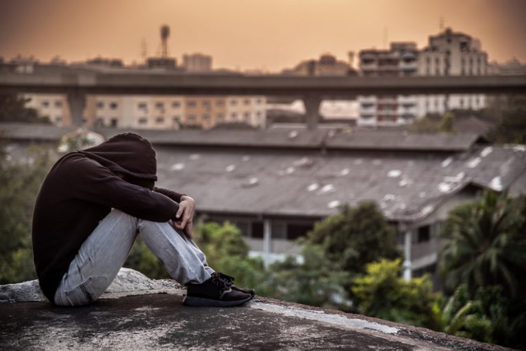 Young Asian man sitting on rooftop of an abandoned building with depression or stressed out during sunset in the city.