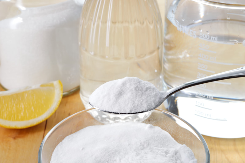 Eco-friendly natural cleaners including vinegar, baking soda, salt, and lemons sit on a wooden table.
