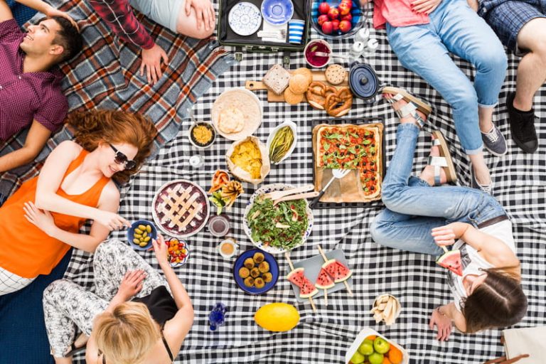 A happy group of friends relaxing on plaid blankets enjoying a picnic together.