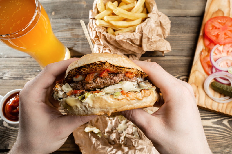 Fast food meal including a burger, fries, and a beer on a wooden table.