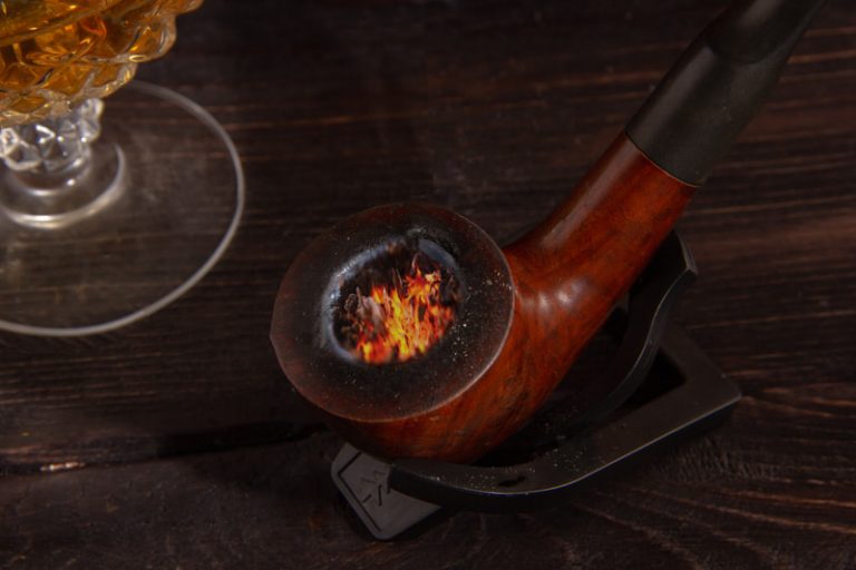 Smoking pipe next to a glass of whiskey on a wooden desk.