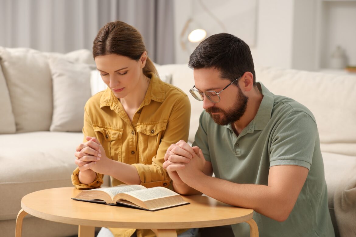 A pastor and his wife praying together at home.