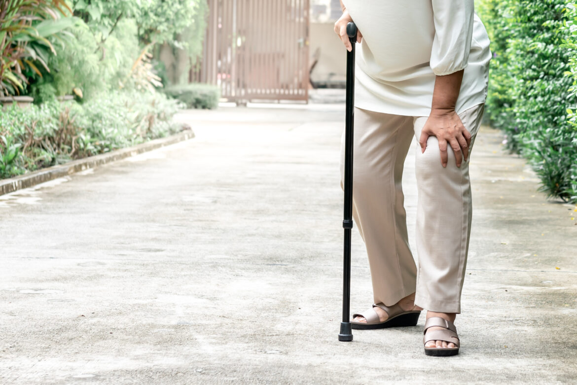 An elderly person walking with a cane.