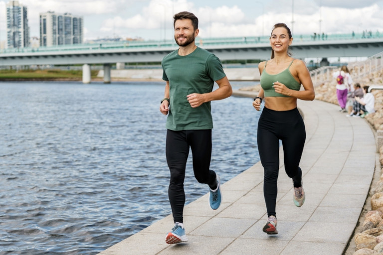 Couple running by a river with a cityscape in the background.