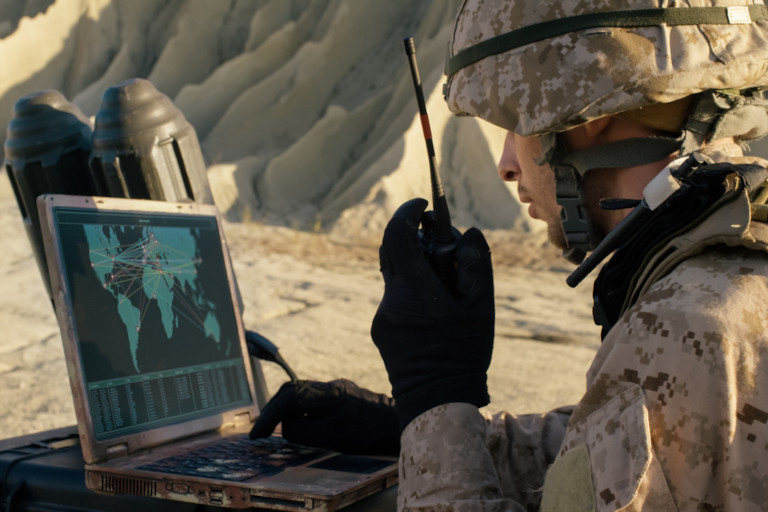 A soldier using a laptop and radio for communication during a military exercise in the desert.