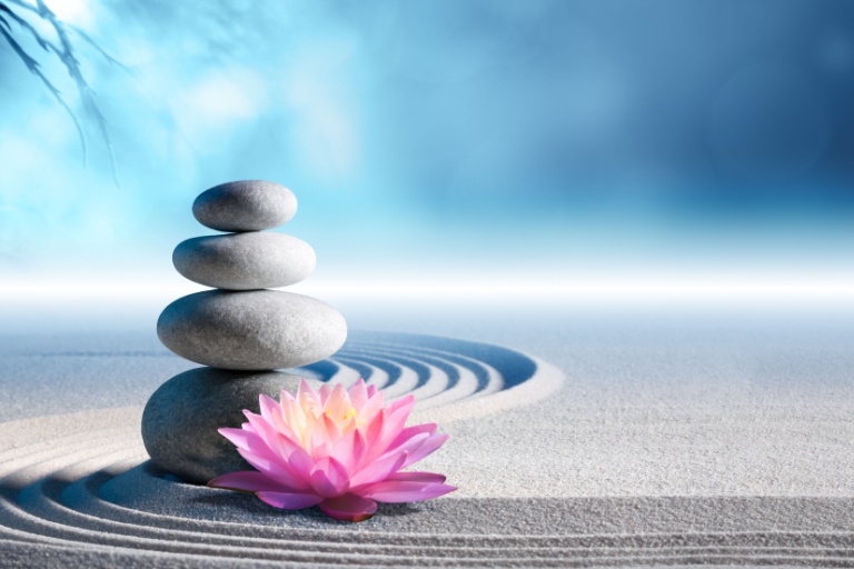 Stacked round rocks, a lotus flower, and wavy lines in the sand.