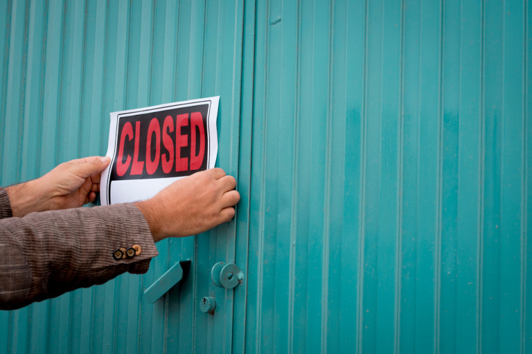 Unrecognizable store owner putting closed sign on the roll-up shutter of a business.