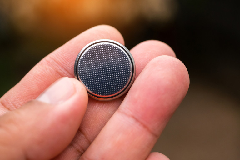 Man holding a button battery in his hand.