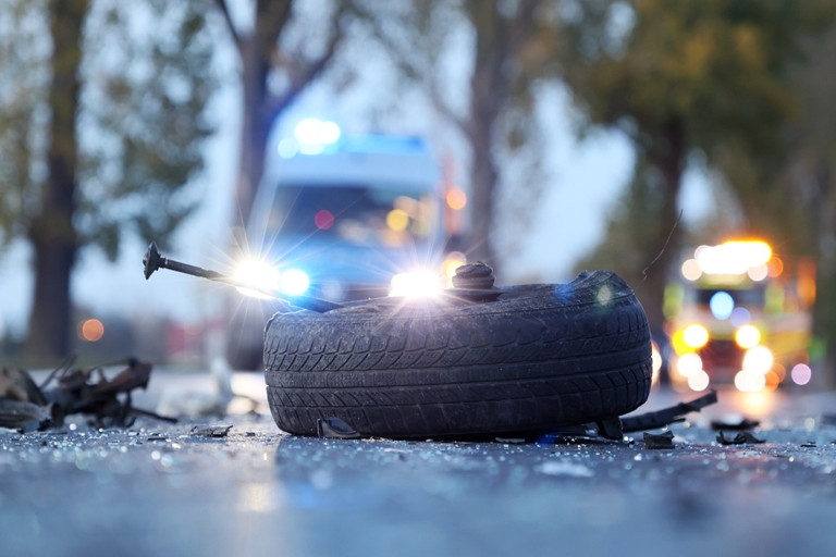 Wreckage from an automobile accident with emergency vehicles in the background.