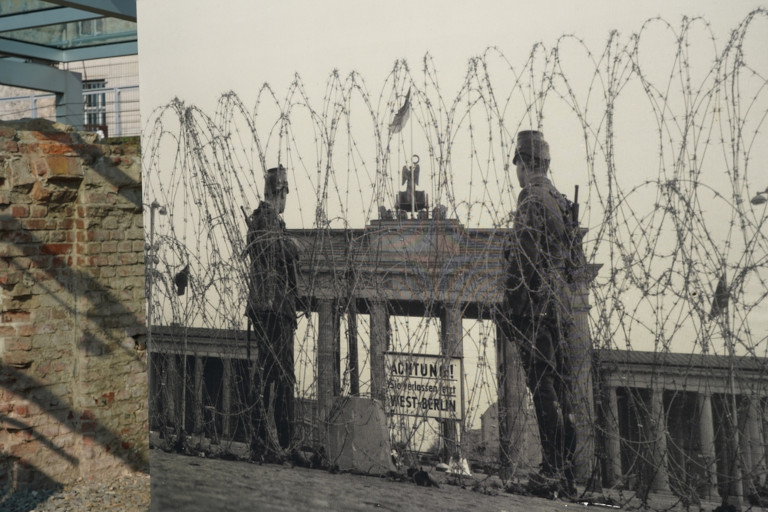 Old photo of Russian soldiers guarding the border between East and West Berlin in the 1960s at the Berlin wall seen through razor-sharp wire.