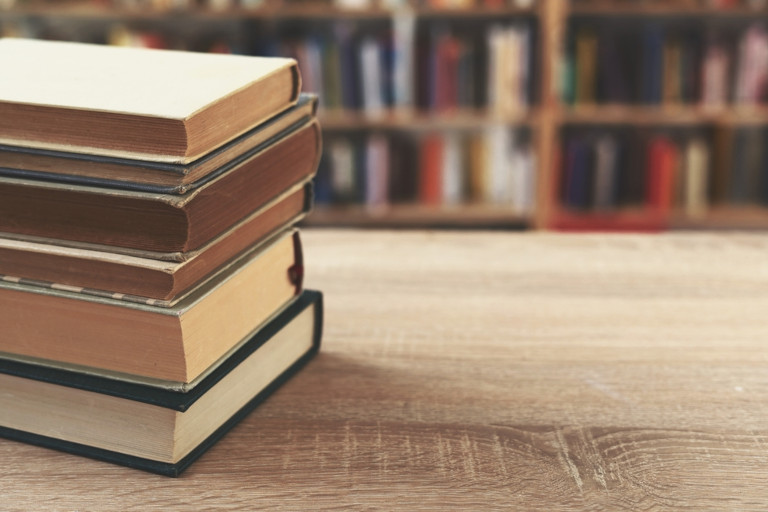 Stack of books on a wooden table in a library.