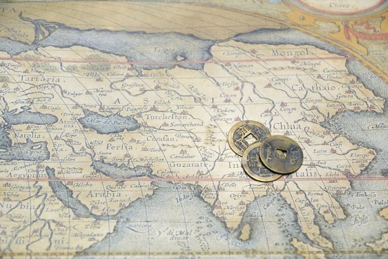 Old map of Asia with ancient Chinese coins laying on top.