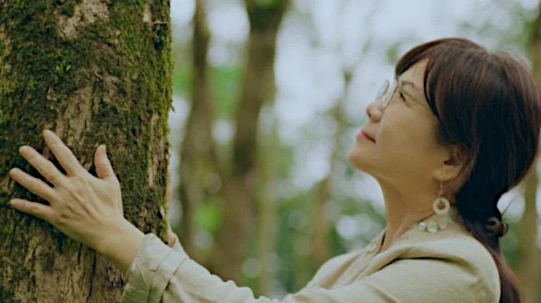 Artist Peng Yamei in a forest by a tree.