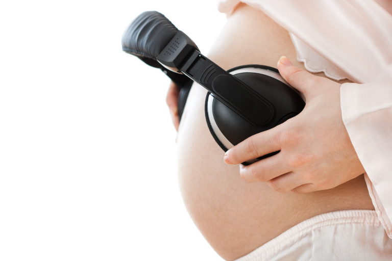 Image of a pregnant woman holding headphones over her belly.