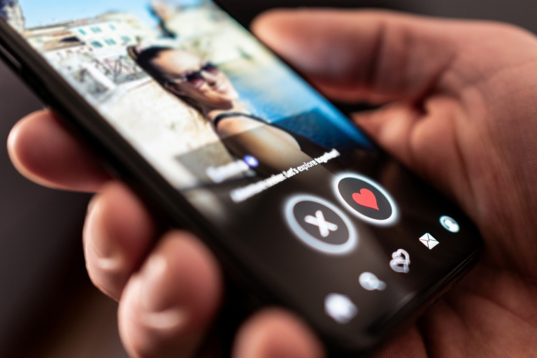 Man holding his smartphone and looking at a woman's profile on a dating app.