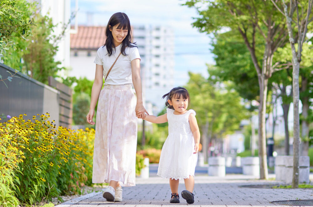 Smiling Asian mother holding her young daughter's hand as they walk down a city street.