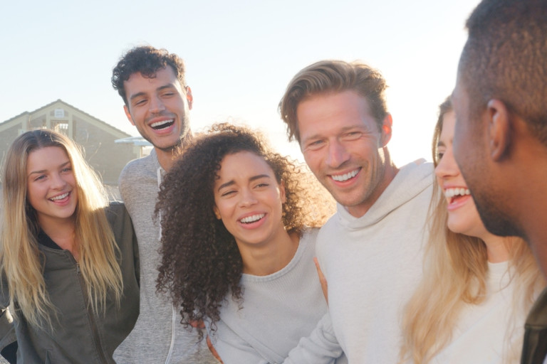 Diverse group of friends embracing and laughing together outdoors on a sunny day.