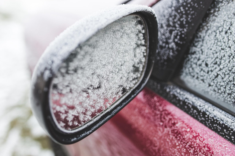 Side mirror on a car outside in winter with snow on it.