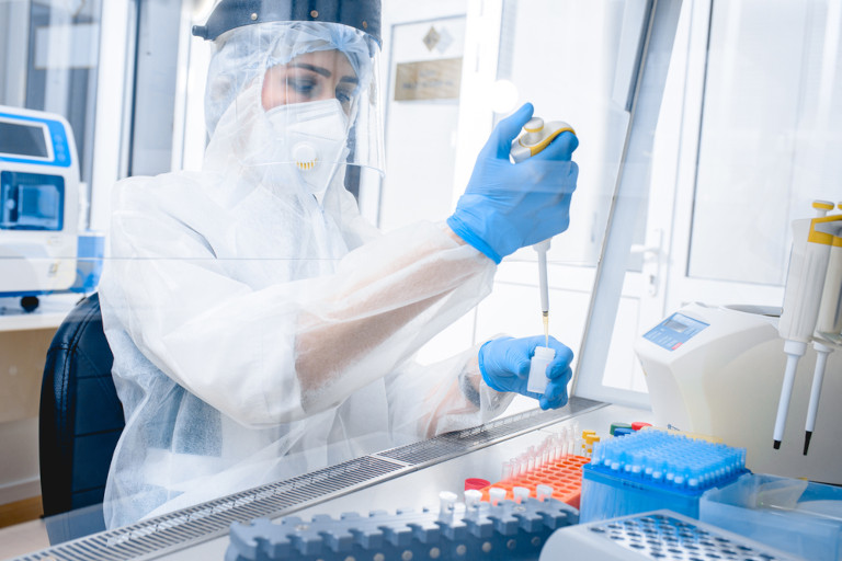 Researcher in protective clothing using a pipette to transfer liquid in a ventilated cabinet.