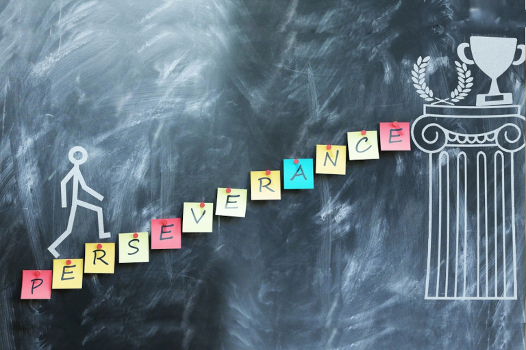 Drawing on a chalkboard of a stick figure climbing stairs to a trophy and laurel resting on a pillar with the word 'perseverance' serving as the steps.