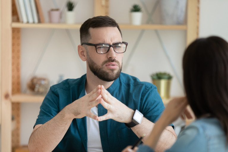 Man with a confused look on his face sitting at a table listening to a young woman explain something.