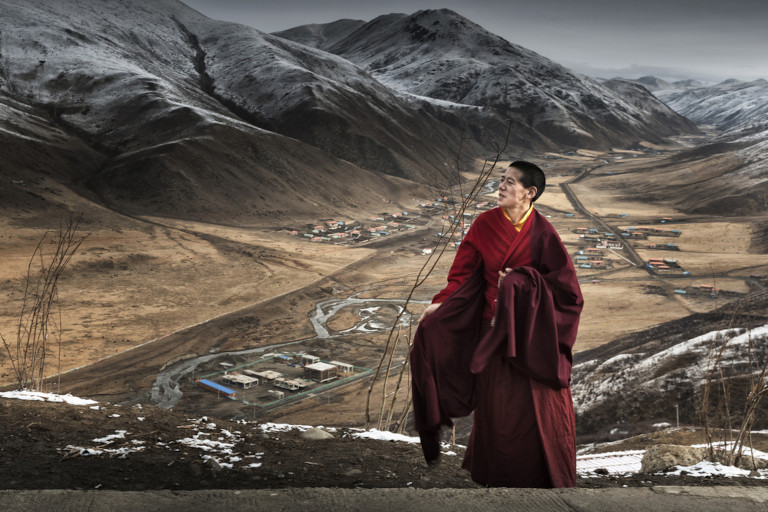Monk standing outside with mountains in the background.