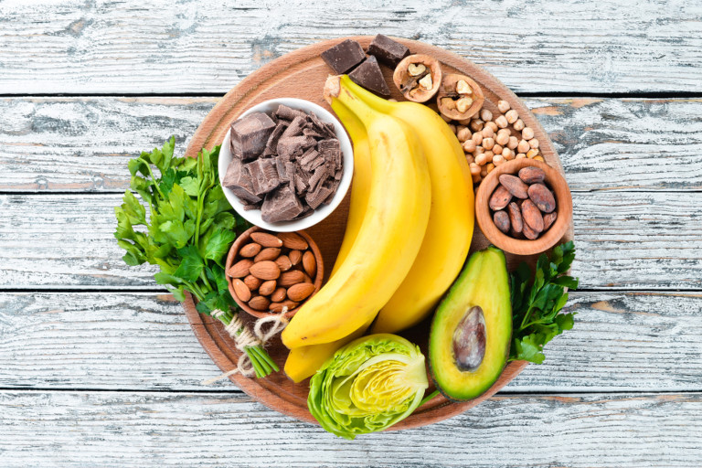 A plate holding potassium-rich foods including bananas, avocados, and almonds.