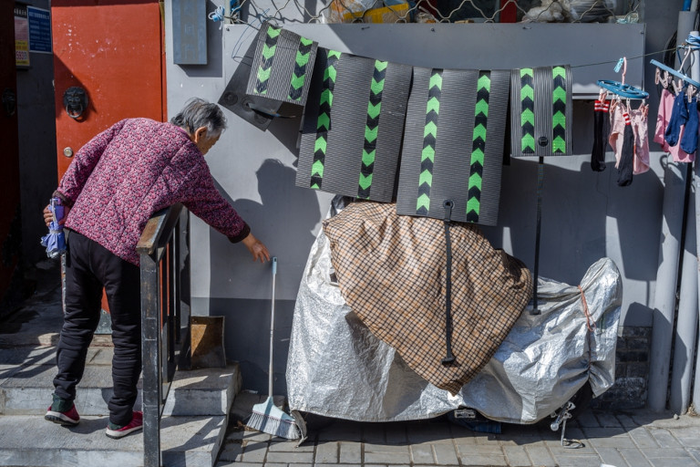 Man cleaning outside in Shanghai by mats hung out to dry in an alleyway.