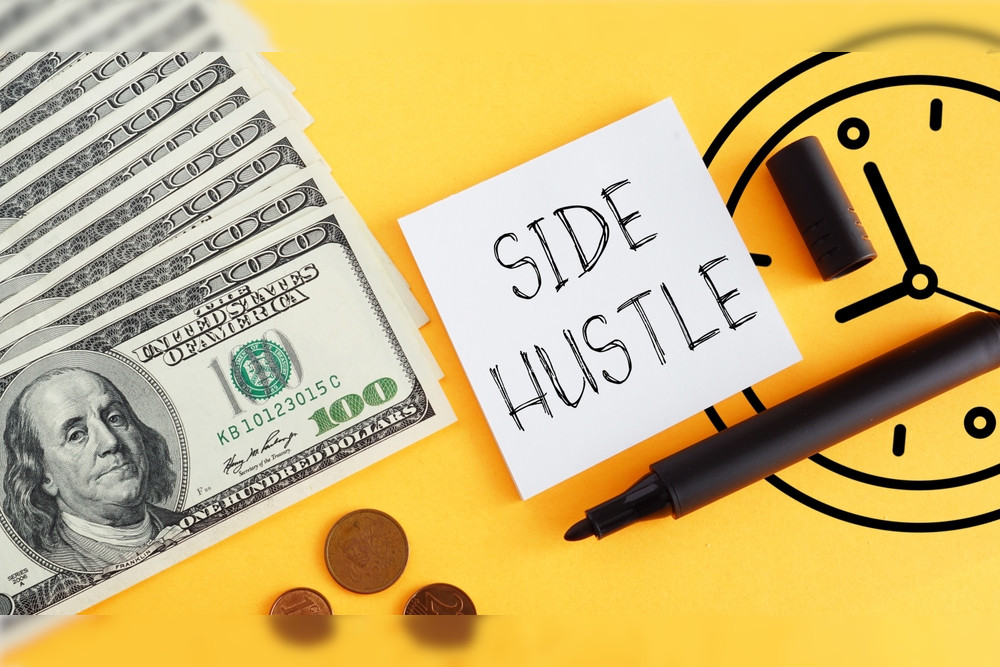 US$100 bills and pennies on a yellow background with a black sharpie and a note that reads 'side hustle.'