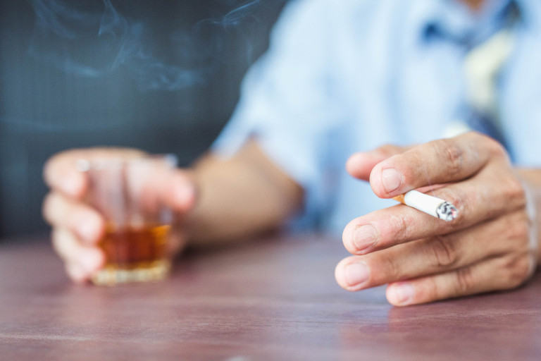 Man sitting with a glass of whiskey and a lit cigarette.