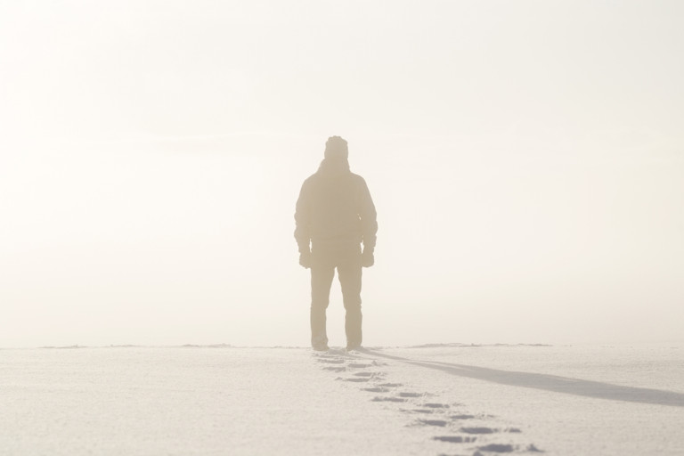Silhouette of a young man standing out in the snow.