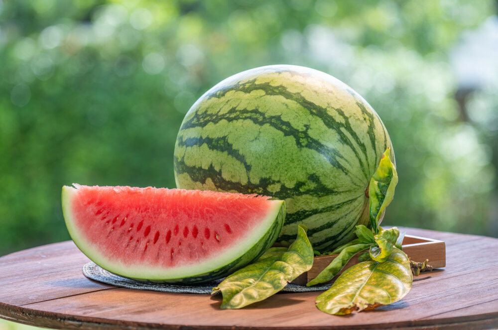Fresh, ripe watermelon on a wooden table outdoors.
