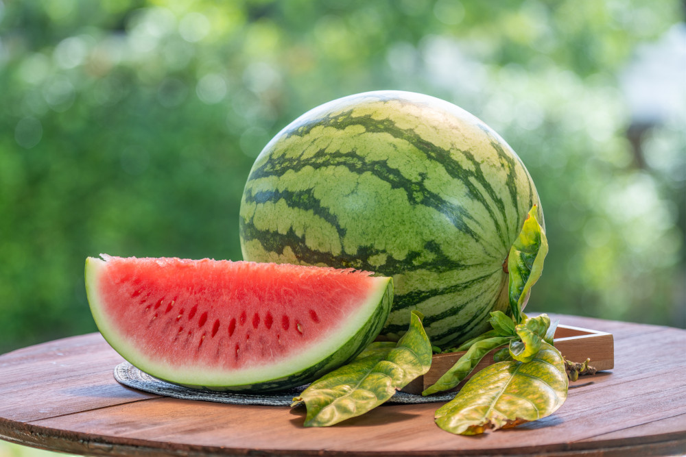 Fresh, ripe watermelon on a wooden table outdoors.