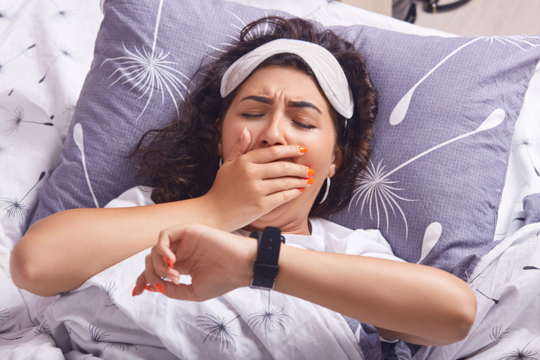 Young woman yawning as she lays in bed.