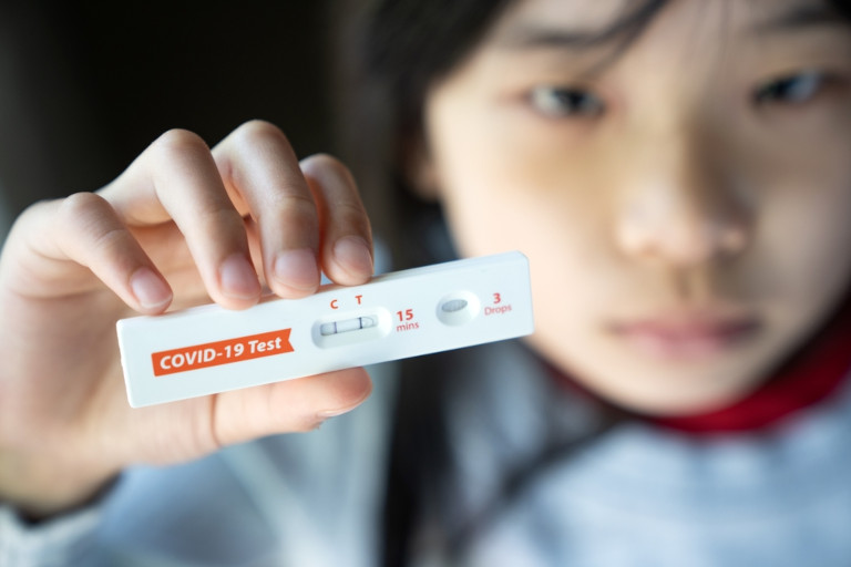 Child holding a COVID test showing a positive result.