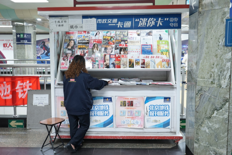 Woman laying out papers at a news stand in Beijing.