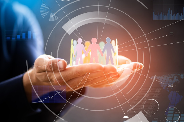 A person holds a group of paper-cutout figures symbolizing community and inclusion, surrounded by digital data graphics representing technology and connection.