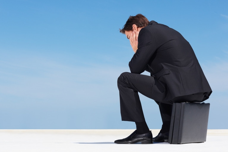 Disappointed businessman sitting on his briefcase outside on the sidewalk.
