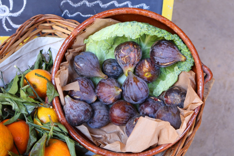 Basket containing fresh figs sitting next to some oranges.