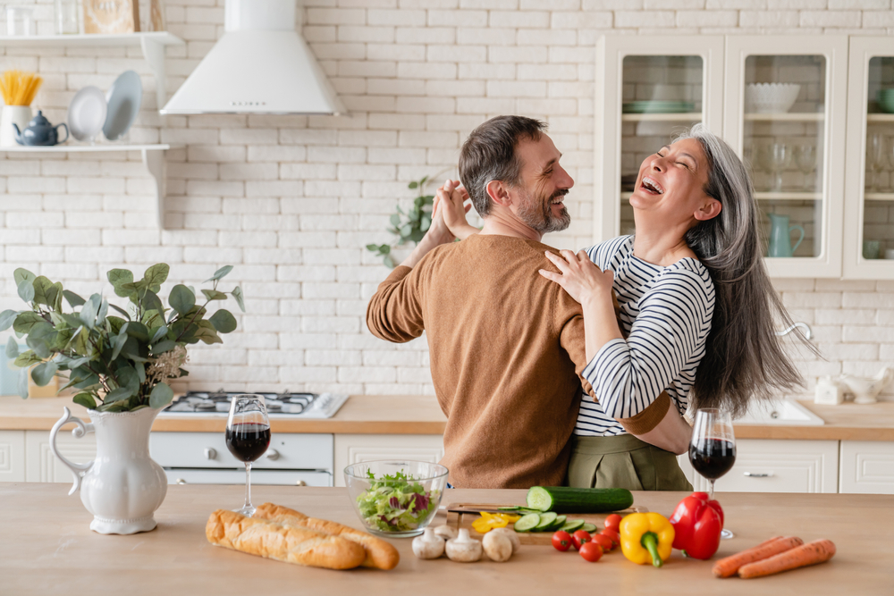 Happy middle-aged couple laughing and dancing together in the kitchen.