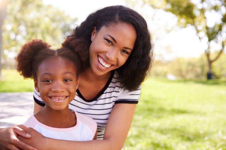 Smiling mother and daughter in a park on a sunny day.