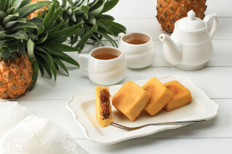 Taiwanese pineapple cake pastry served on a white plate sitting next to a whole pineapple and two cups filled with tea.