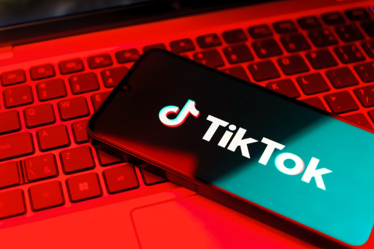 TikTok logo on a smartphone sitting on a laptop bathed in red light.