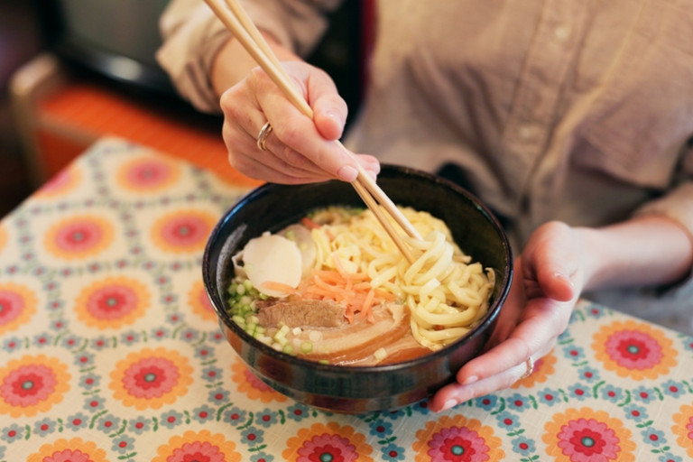 Woman eating a bowl of ramen with chopsticks in a restaurant.