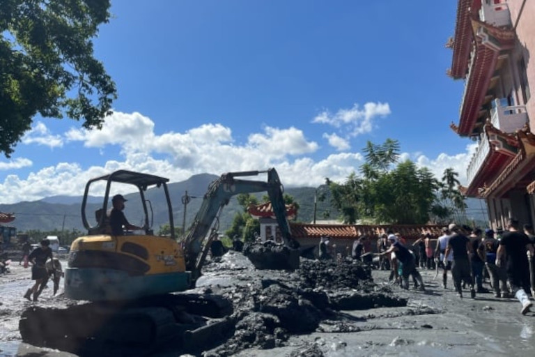 Volunteers using wheelbarrows to dump mud so it can be hauled away by heavy equipment after a disaster in Taiwan.