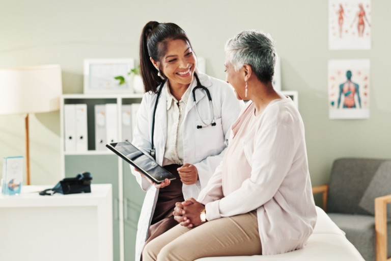 Mature patient smiling as a doctor shows her something on a tablet.