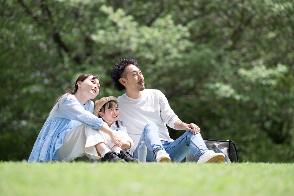 Young Japanese couple with their child on a blanket at the park.