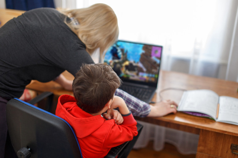 Parent reaching for the mouse as her son sits in front of a computer with the Roblox game on the screen.