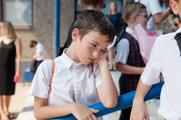 Sad schoolboy standing outside alone as other children talk to each friends.